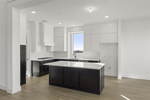 kitchen with white cabinets, light wood-type flooring, a kitchen island, and sink