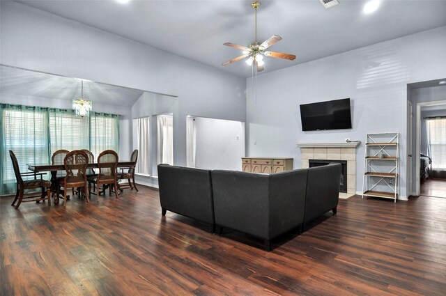 living room featuring ceiling fan with notable chandelier, a tiled fireplace, and dark hardwood / wood-style flooring