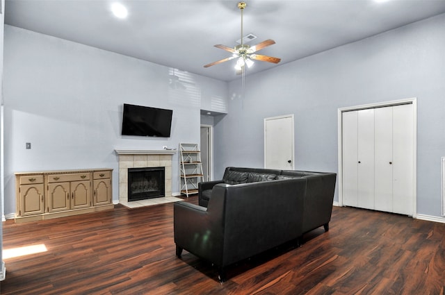 living room featuring dark wood-type flooring, ceiling fan, a tiled fireplace, and a towering ceiling