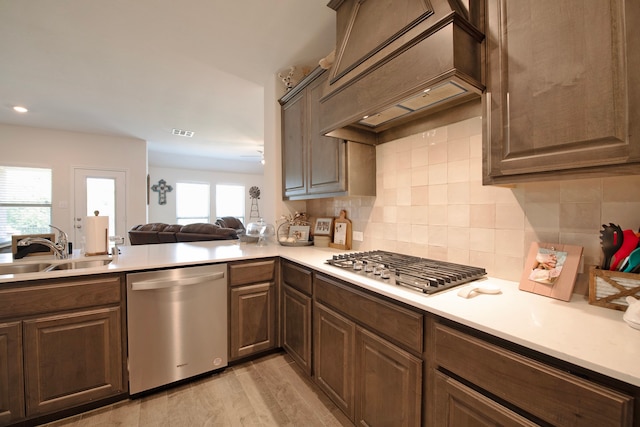 kitchen with tasteful backsplash, kitchen peninsula, sink, appliances with stainless steel finishes, and light hardwood / wood-style floors