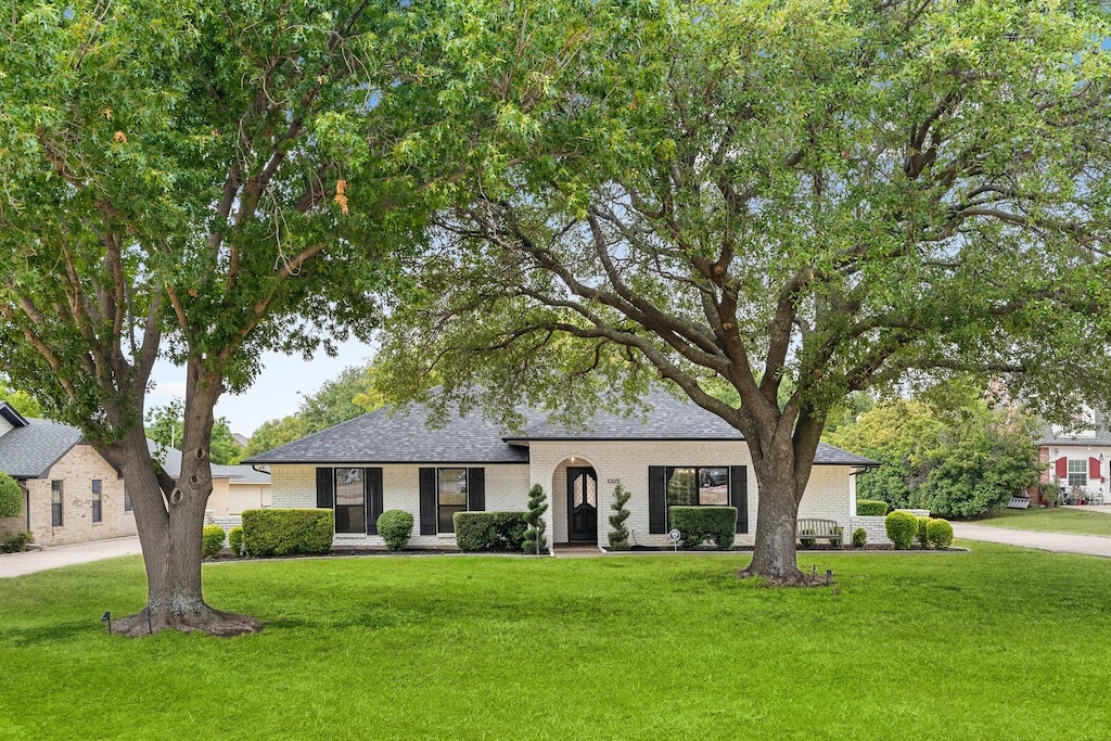 view of front of home with a shingled roof, a front lawn, and brick siding