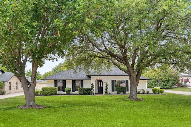 view of front of home with a shingled roof, a front lawn, and brick siding