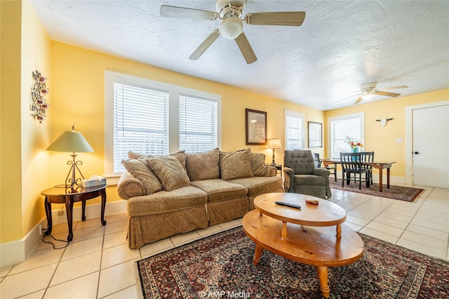 living room with a ceiling fan, a textured ceiling, baseboards, and light tile patterned floors