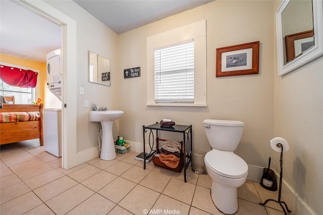 bathroom featuring stacked washer and clothes dryer, toilet, a sink, tile patterned flooring, and baseboards