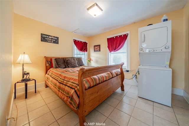 bedroom with baseboards, light tile patterned flooring, attic access, and stacked washer / drying machine