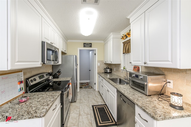 kitchen with tasteful backsplash, light stone counters, appliances with stainless steel finishes, white cabinetry, and sink