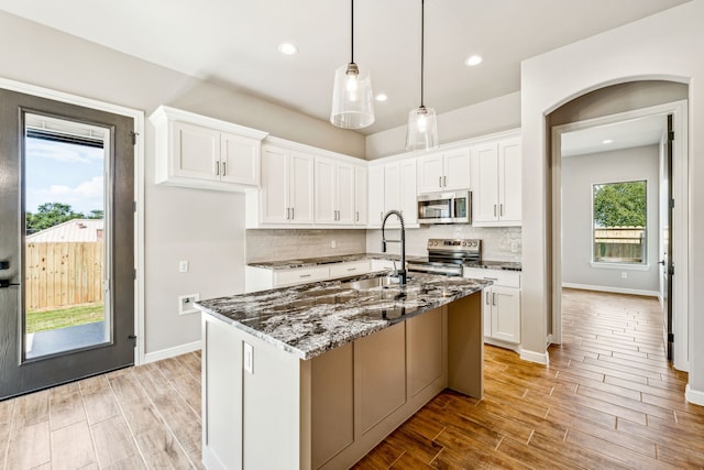 kitchen with wood finish floors, dark stone counters, appliances with stainless steel finishes, white cabinets, and a sink