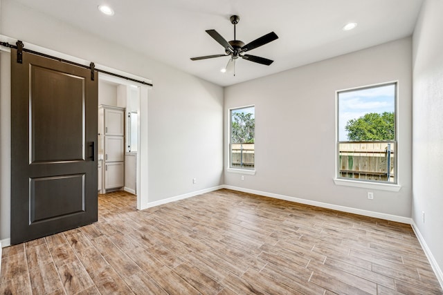 empty room with a barn door, ceiling fan, light wood-type flooring, and a healthy amount of sunlight