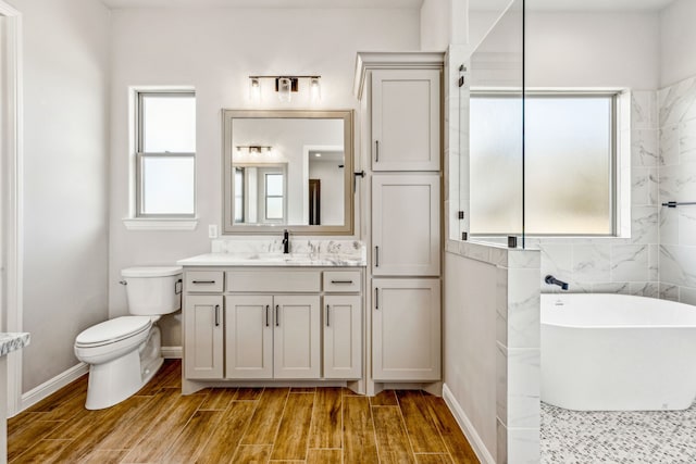 bathroom featuring vanity, wood finished floors, baseboards, a soaking tub, and toilet