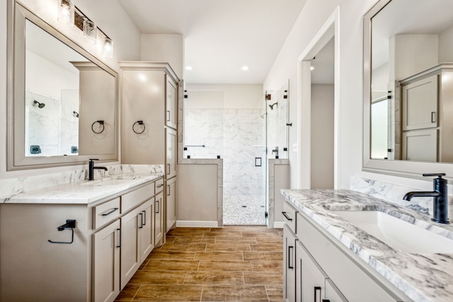 bathroom featuring wood finish floors, two vanities, a marble finish shower, and a sink