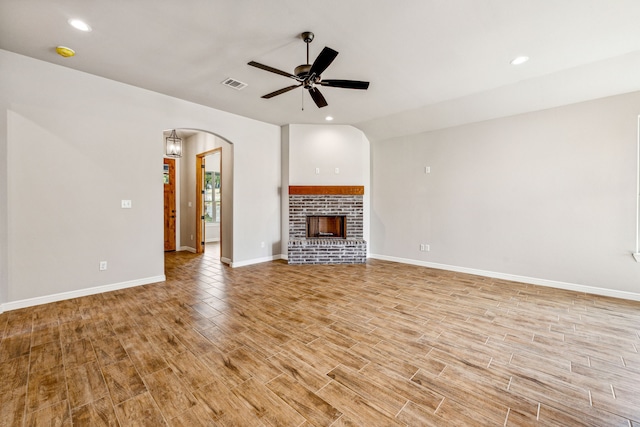 unfurnished living room with a ceiling fan, visible vents, light wood finished floors, a fireplace, and arched walkways