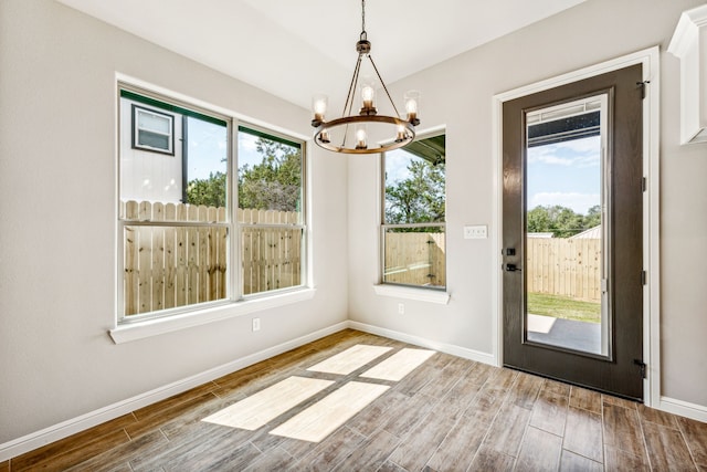 unfurnished dining area featuring an inviting chandelier, baseboards, and wood finish floors