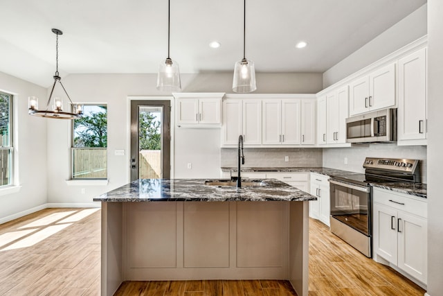 kitchen featuring appliances with stainless steel finishes, a kitchen island with sink, tasteful backsplash, sink, and dark stone counters