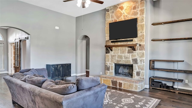 living room with a stone fireplace, a towering ceiling, dark hardwood / wood-style floors, and ceiling fan