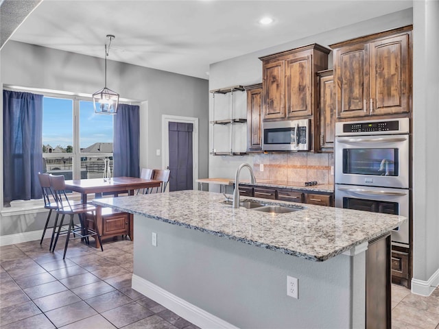 kitchen featuring a kitchen island with sink, sink, stainless steel appliances, backsplash, and decorative light fixtures