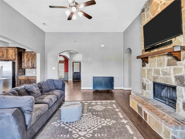 living room featuring ceiling fan, a stone fireplace, and dark wood-type flooring