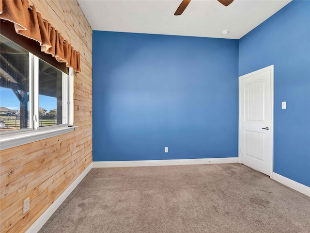 empty room featuring carpet flooring, wood walls, and ceiling fan