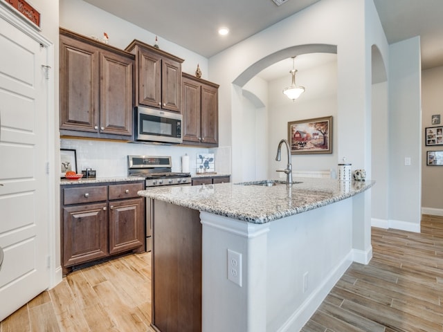 kitchen with light stone countertops, appliances with stainless steel finishes, decorative backsplash, dark brown cabinetry, and sink