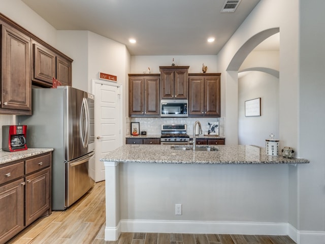 kitchen featuring backsplash, light stone counters, sink, and appliances with stainless steel finishes