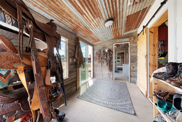 interior space with wooden walls, wooden ceiling, a barn door, carpet flooring, and lofted ceiling