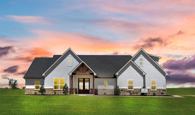 modern farmhouse featuring stone siding, a front yard, french doors, and roof with shingles