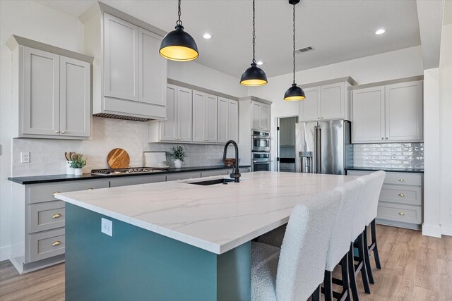 kitchen featuring stainless steel appliances, decorative light fixtures, light wood-type flooring, and a kitchen island with sink