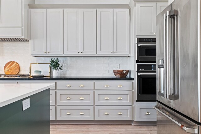 kitchen featuring light hardwood / wood-style floors, appliances with stainless steel finishes, dark stone counters, and tasteful backsplash