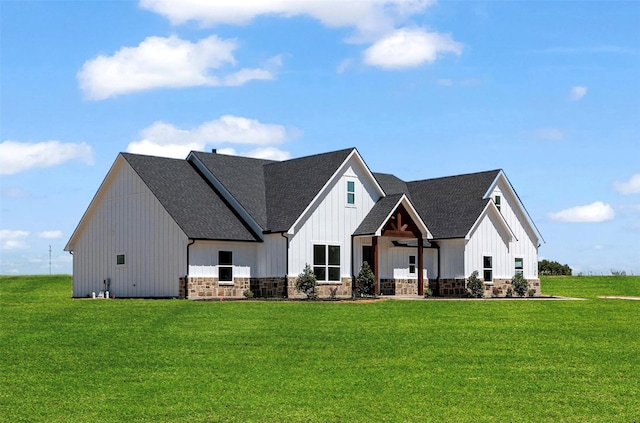 back of property with board and batten siding, stone siding, roof with shingles, and a yard