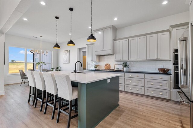 kitchen with light hardwood / wood-style flooring, a breakfast bar area, pendant lighting, a center island with sink, and tasteful backsplash