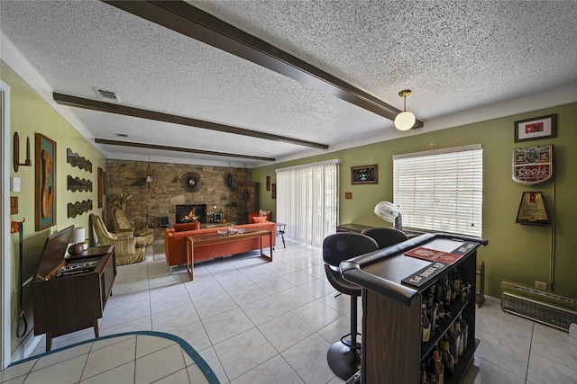 interior space featuring beam ceiling, a stone fireplace, and a textured ceiling