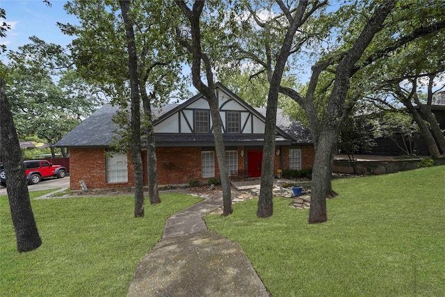 tudor house featuring roof with shingles, a front yard, and brick siding