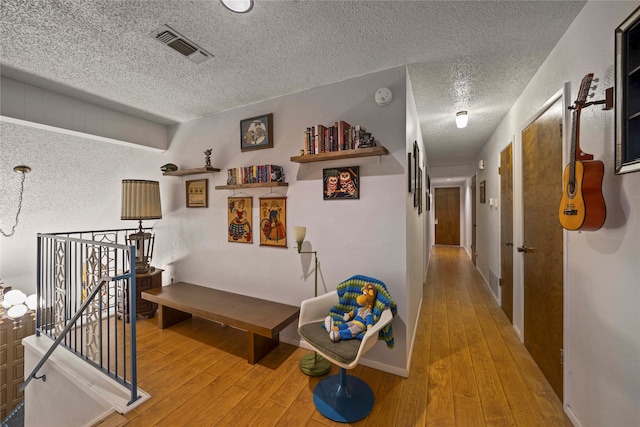 corridor with hardwood / wood-style floors, a textured ceiling, and an inviting chandelier