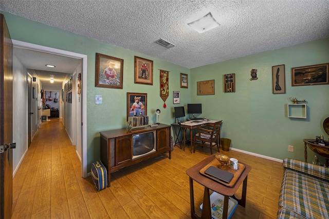 home office with light wood-type flooring and a textured ceiling