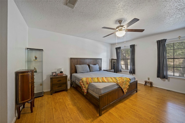 bedroom featuring a textured ceiling, light hardwood / wood-style floors, multiple windows, and ceiling fan