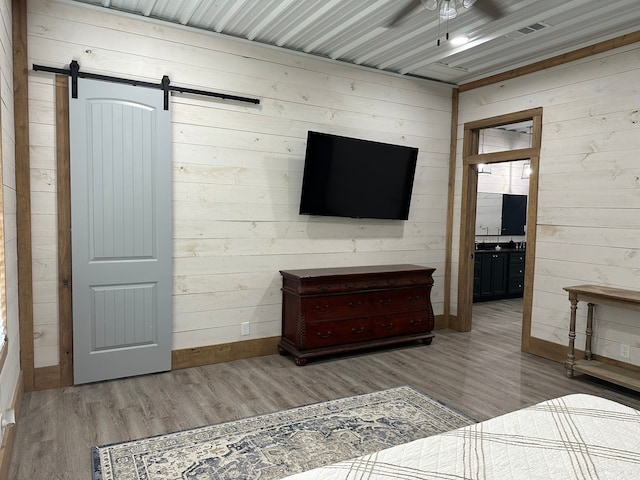 bedroom with a barn door, ensuite bath, light hardwood / wood-style flooring, and wooden walls