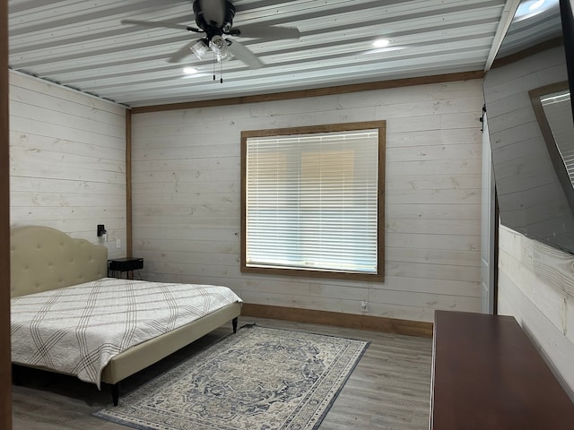 bedroom featuring ceiling fan, hardwood / wood-style floors, and wooden walls