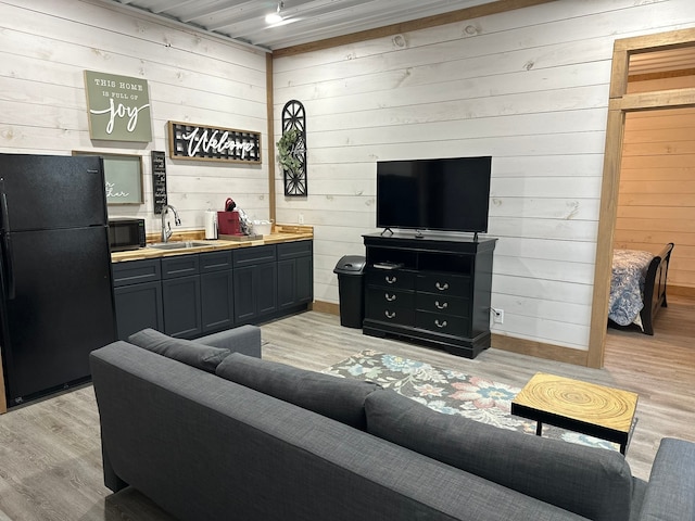 living room with light hardwood / wood-style flooring, sink, and wooden walls