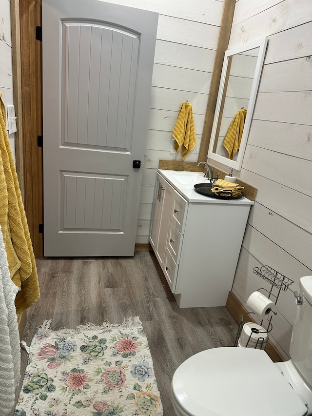 bathroom featuring vanity, toilet, wood-type flooring, and wooden walls