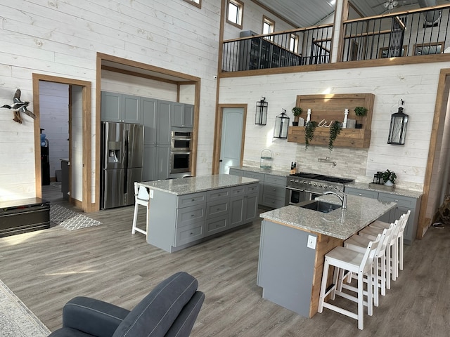 kitchen with light stone counters, stainless steel appliances, a high ceiling, a kitchen bar, and a kitchen island with sink