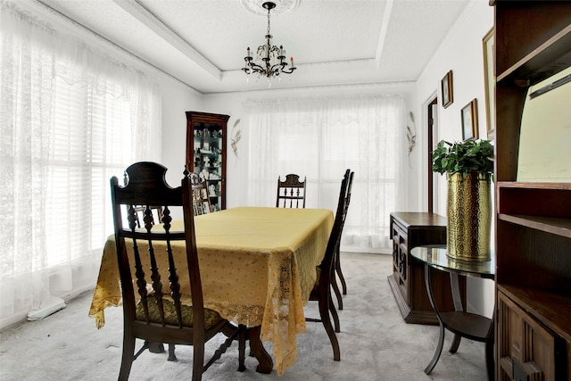 dining area with a textured ceiling, light carpet, a chandelier, and a tray ceiling