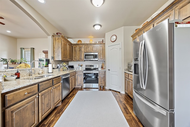 kitchen featuring stainless steel appliances, sink, light stone countertops, ceiling fan, and dark wood-type flooring