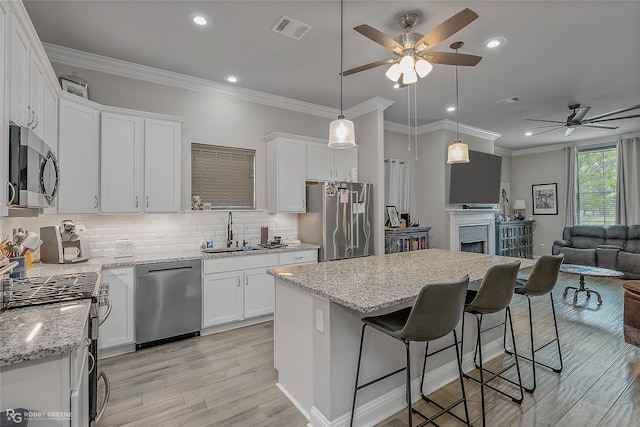 kitchen with visible vents, appliances with stainless steel finishes, open floor plan, white cabinetry, and a sink