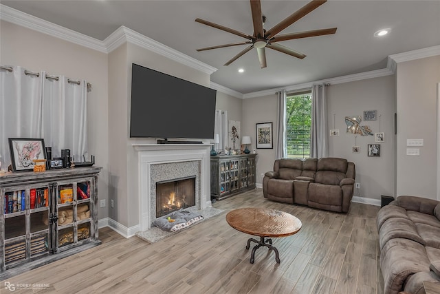 living room featuring a warm lit fireplace, baseboards, ornamental molding, and wood finished floors