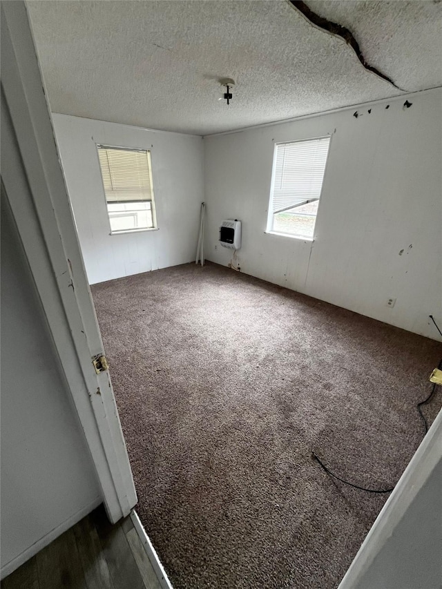 carpeted spare room featuring heating unit, a wealth of natural light, and a textured ceiling