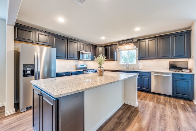 kitchen featuring light stone countertops, stainless steel appliances, sink, light hardwood / wood-style flooring, and a kitchen island