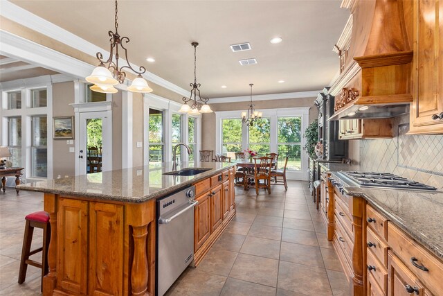 kitchen featuring decorative light fixtures, a kitchen island with sink, ornamental molding, sink, and dark stone countertops