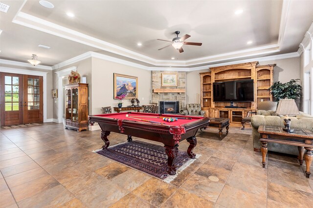 playroom featuring billiards, a raised ceiling, ceiling fan, and a stone fireplace