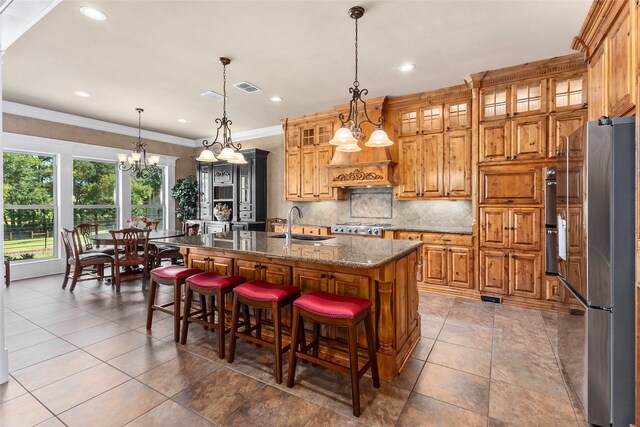 kitchen with pendant lighting, an island with sink, crown molding, stainless steel appliances, and dark stone counters