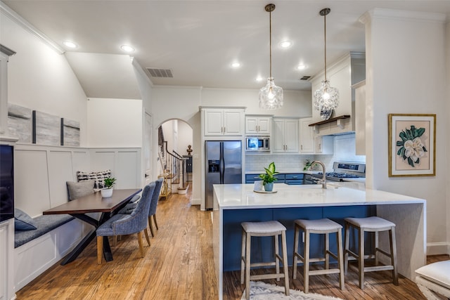 kitchen featuring appliances with stainless steel finishes, light hardwood / wood-style floors, a breakfast bar area, pendant lighting, and ornamental molding