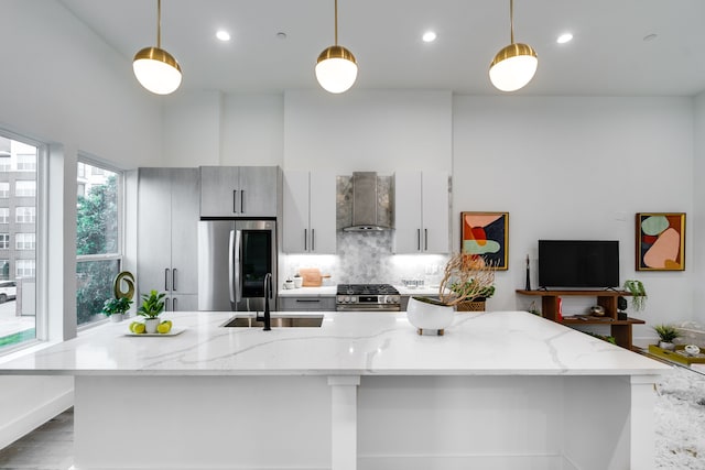 kitchen with appliances with stainless steel finishes, light stone counters, sink, wall chimney exhaust hood, and tasteful backsplash